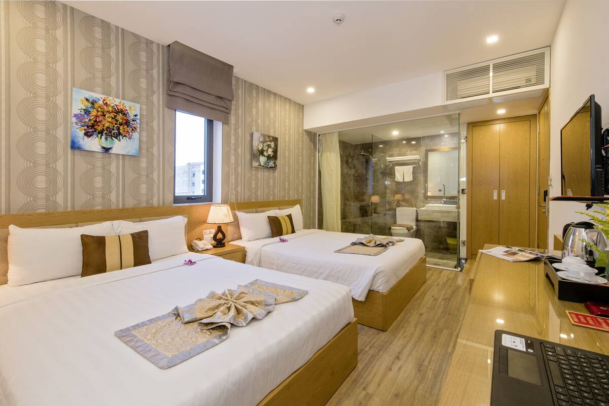 Habitación de hotel con dos camas, un escritorio con una computadora portátil, un televisor y zona de ducha.
