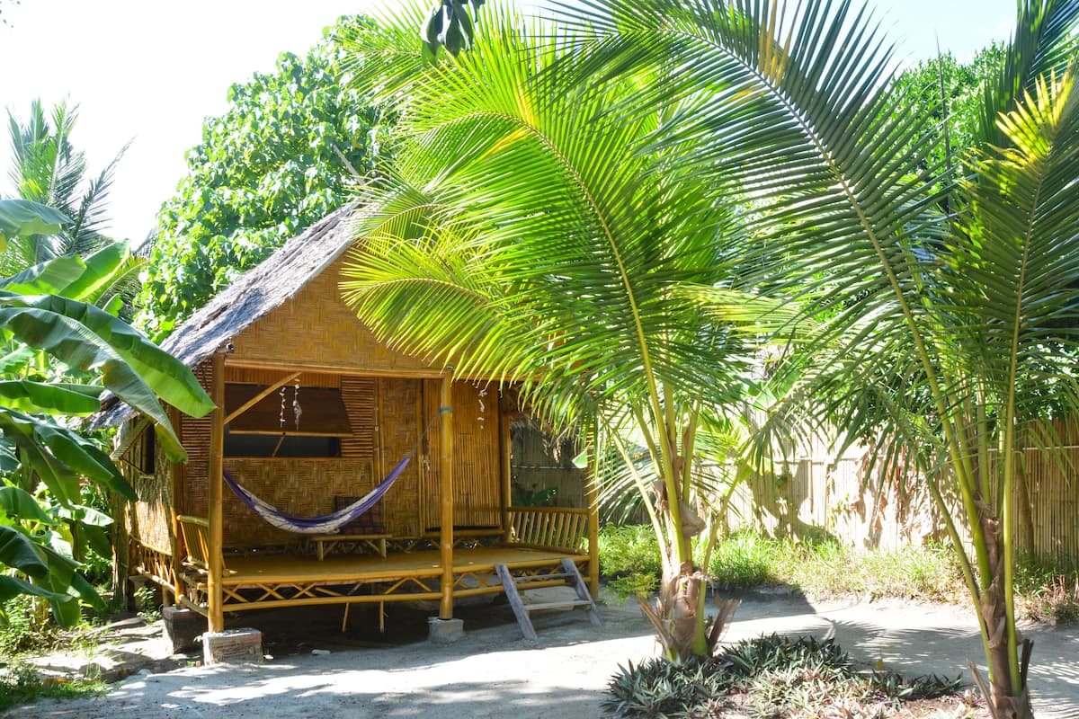 Une cabane rustique en bambou, dotée d’un hamac, entourée d’une végétation tropicale luxuriante.