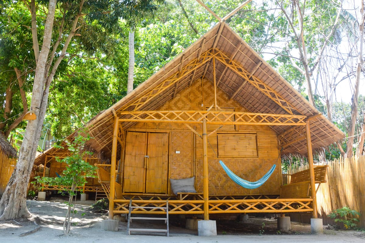 Une structure en bambou surmontée d’un toit de chaume, avec un hamac et une échelle menant à une plateforme surélevée.
