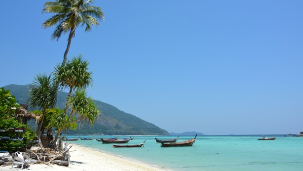 A beach with palm trees, boats, and a mountain in the background. - Forra Diving Resort - Sunrise Beach - Koh Lipe (Koh Lipe)