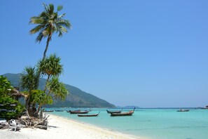 Una playa con palmeras, barcos y una montaña al fondo.