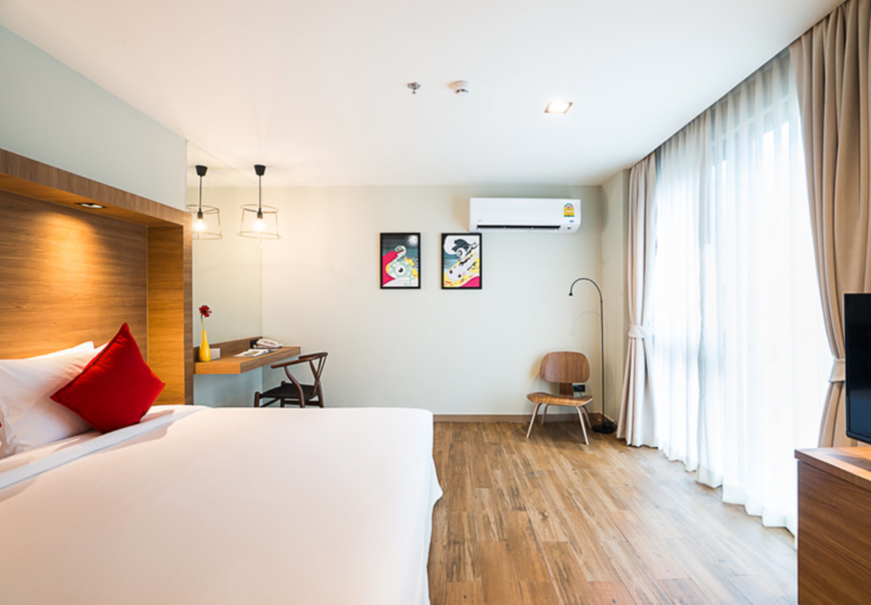 A hotel room with a large bed, a desk, a chair, an air conditioning unit, and a TV.