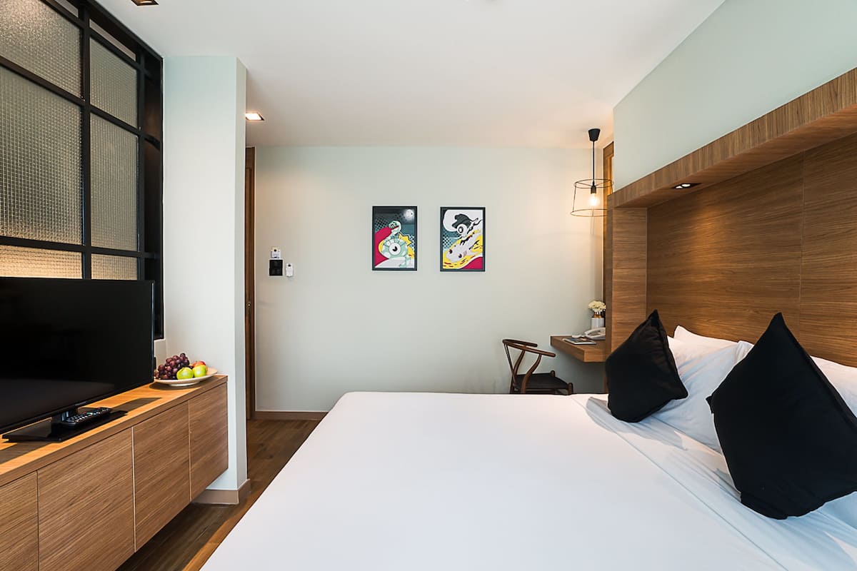 A modern hotel room with a large bed, a TV, a wooden desk, and two artwork pieces on the wall.