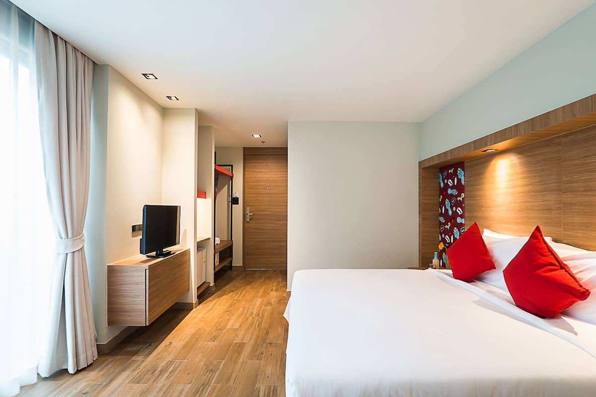 A hotel room with a bed, a TV on a wooden nightstand, a wardrobe, and a door leading to a hallway.