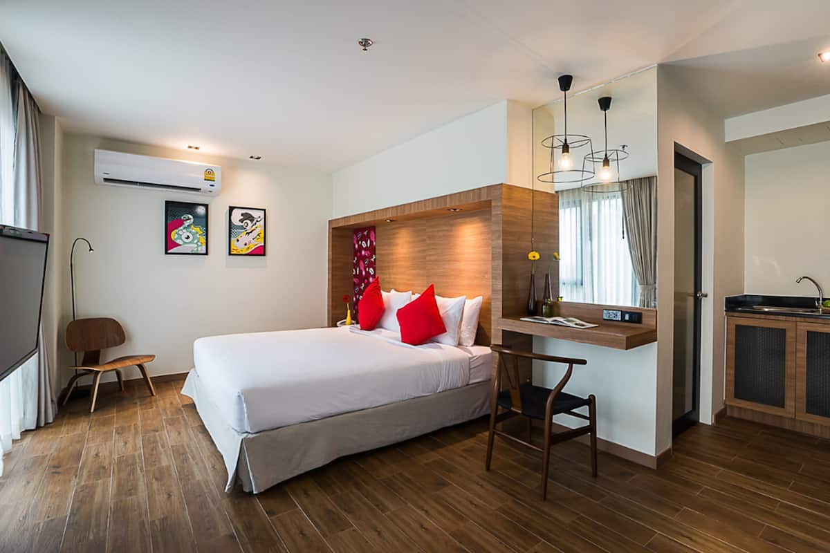 A modern hotel room with a large bed, a desk, and a kitchenette.