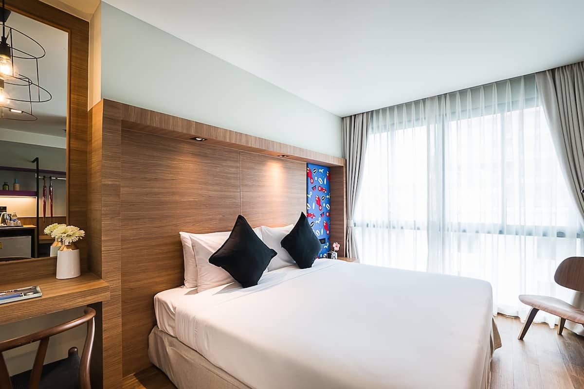 A hotel room with a large bed, a desk, a chair, a mirror, and a window with curtains.