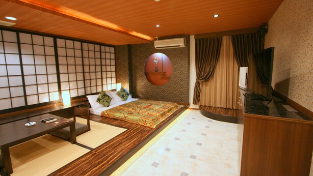 Un dormitorio de estilo japonés tradicional con suelo de tatami, una cama de madera baja, un futón, un escritorio de madera y un divisor de puertas shoji.