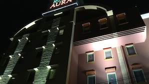 Un hotel llamado "Hotel Aura" con diseño moderno, que presenta un letrero llamativo y varias ventanas iluminadas.