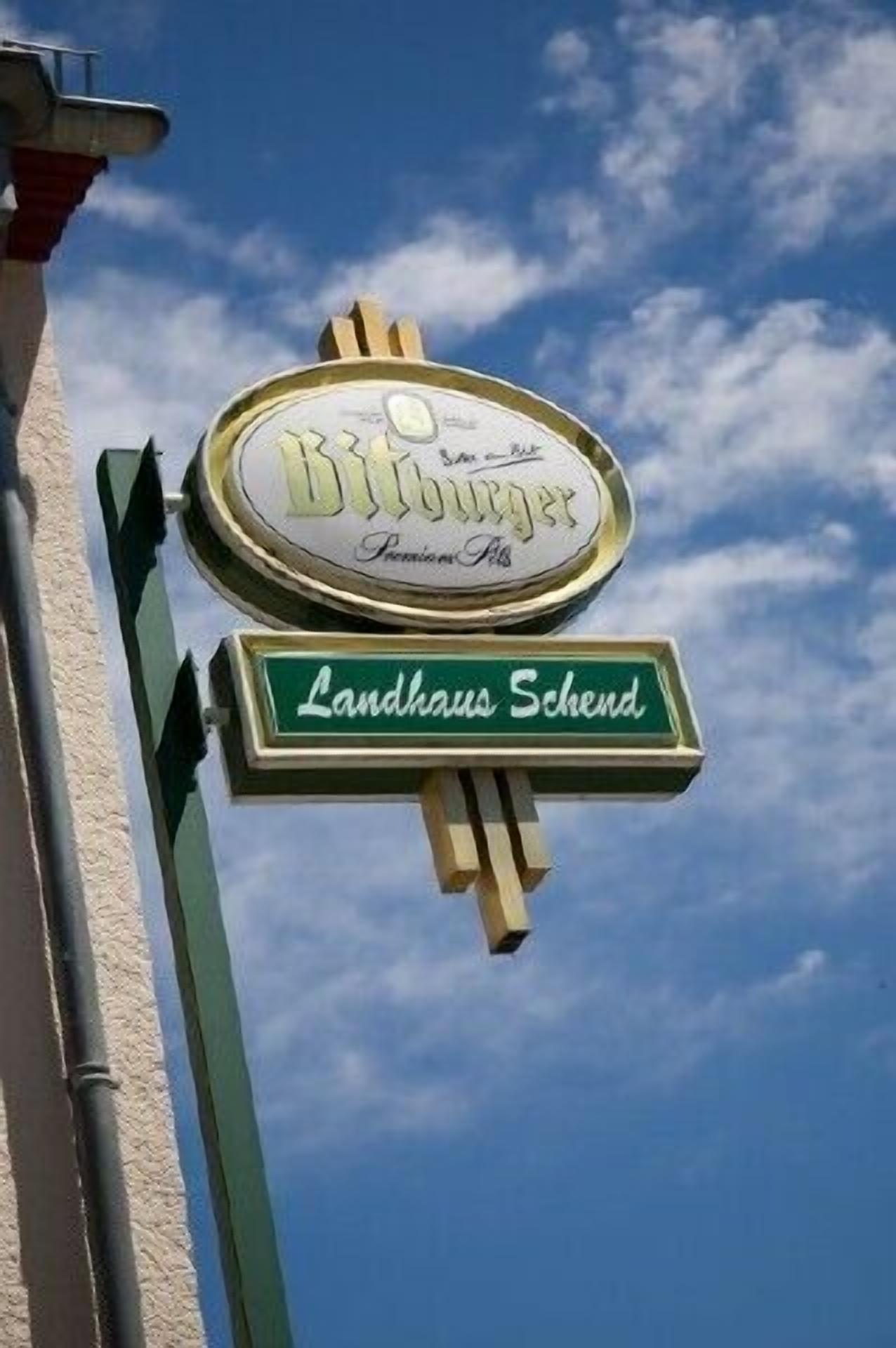 Een bord met 'Bitburger Premium Beer' en 'Landhaus Schied' tegen een helderblauwe lucht.