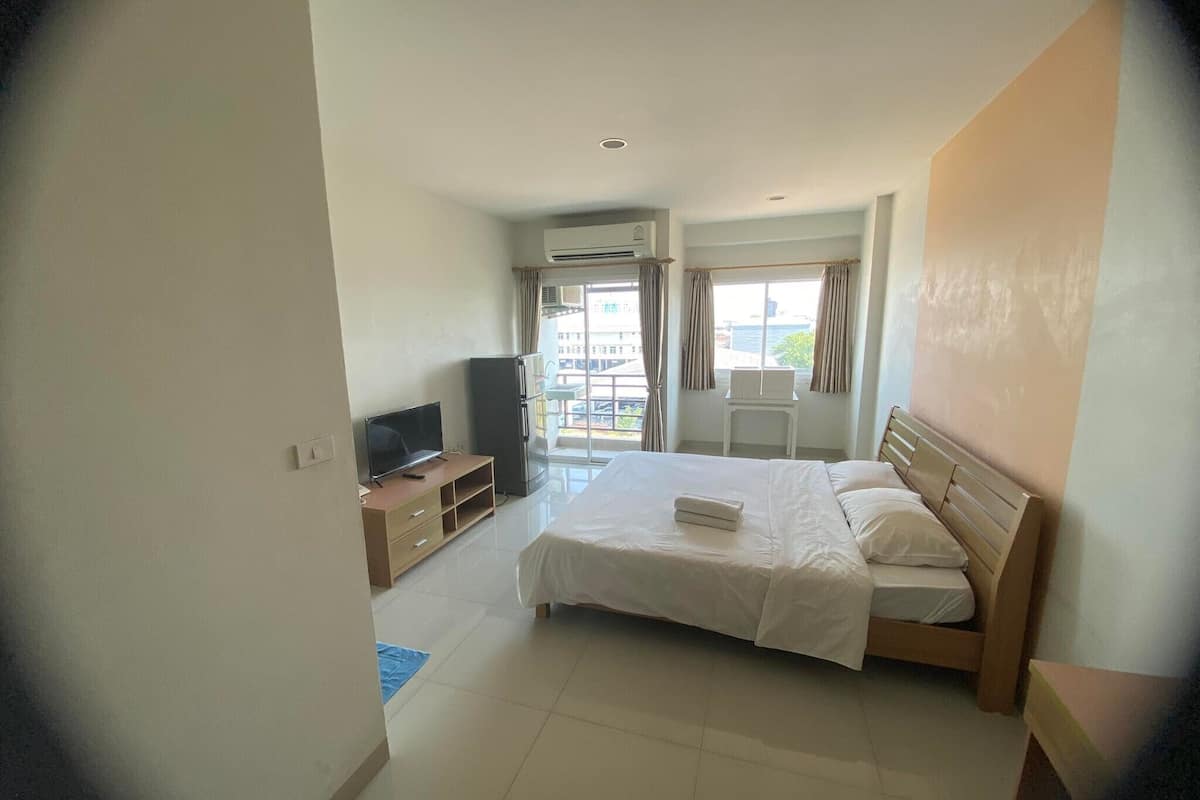 Habitación de hotel con cama, televisión, refrigerador y ventana con cortinas.