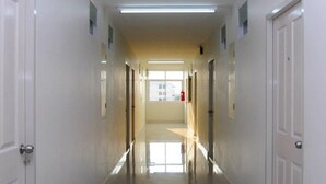 Un long couloir étroit aux murs blancs, avec des portes de chaque côté, qui mène à une pièce lumineuse dotée d’une grande fenêtre.