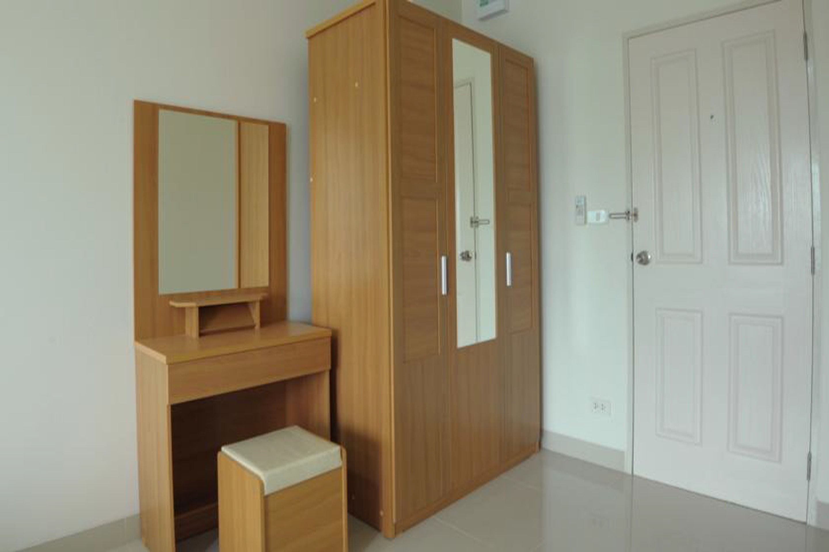 A room with a wooden desk, a mirror, a wardrobe, and a door.