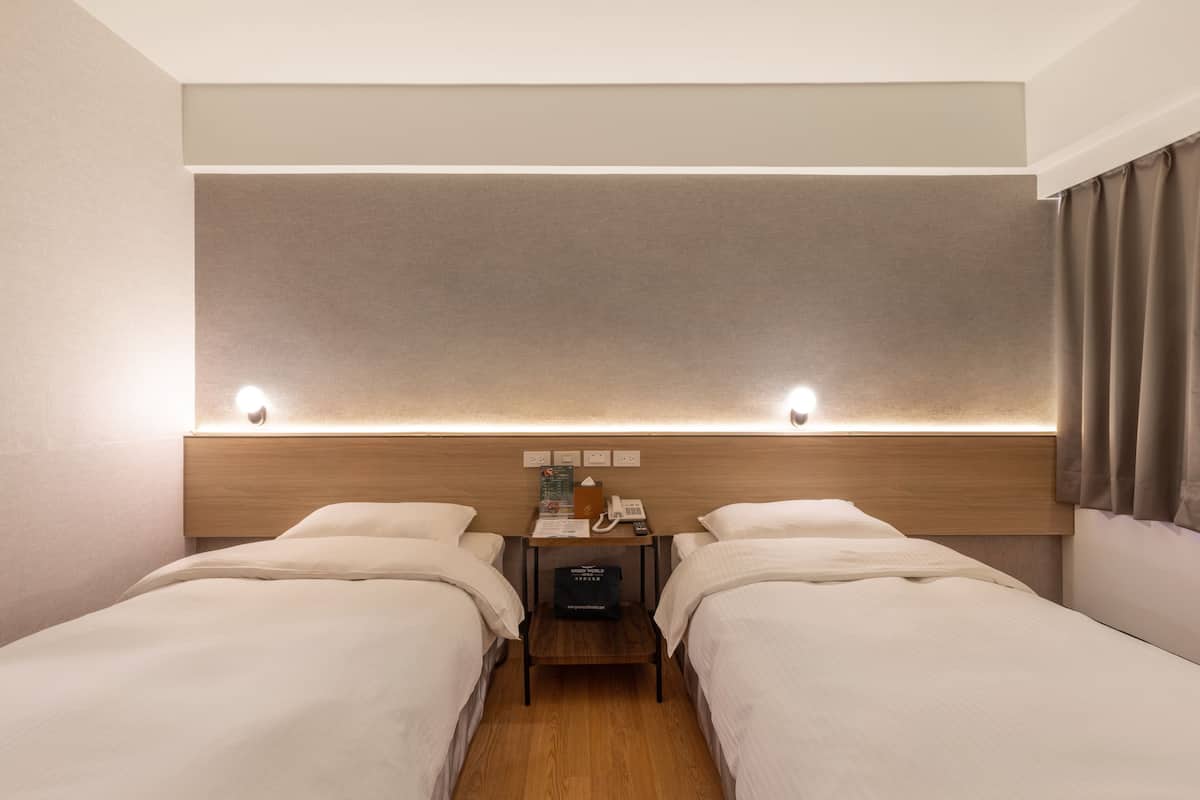 A hotel room with two beds, a wooden headboard, a nightstand with a phone and a lamp, and a small table with a book and a box.