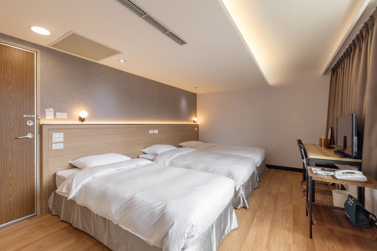 A hotel room with two beds, a desk, a chair, a television, and a window with curtains.