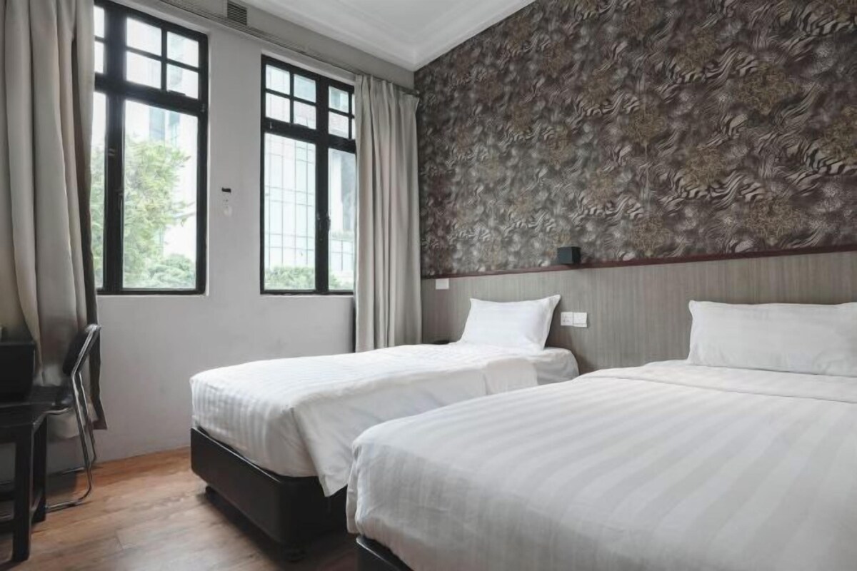 A hotel room with two beds, a desk, and a large window with curtains.