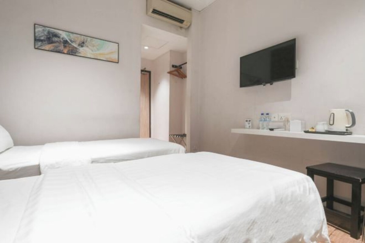 A hotel room with two beds, a mounted TV, a small table with a kettle, and a painting on the wall.