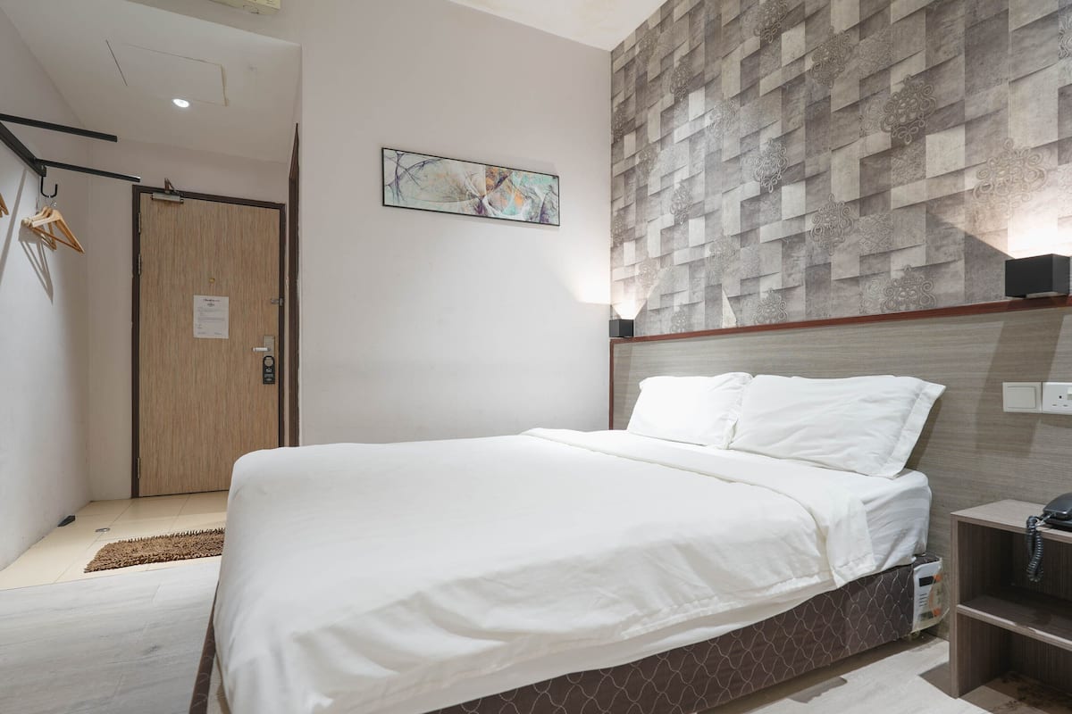 Quarto de hotel moderno com uma cama bem arrumada, porta de madeira, obra de arte na parede e parede estampada.