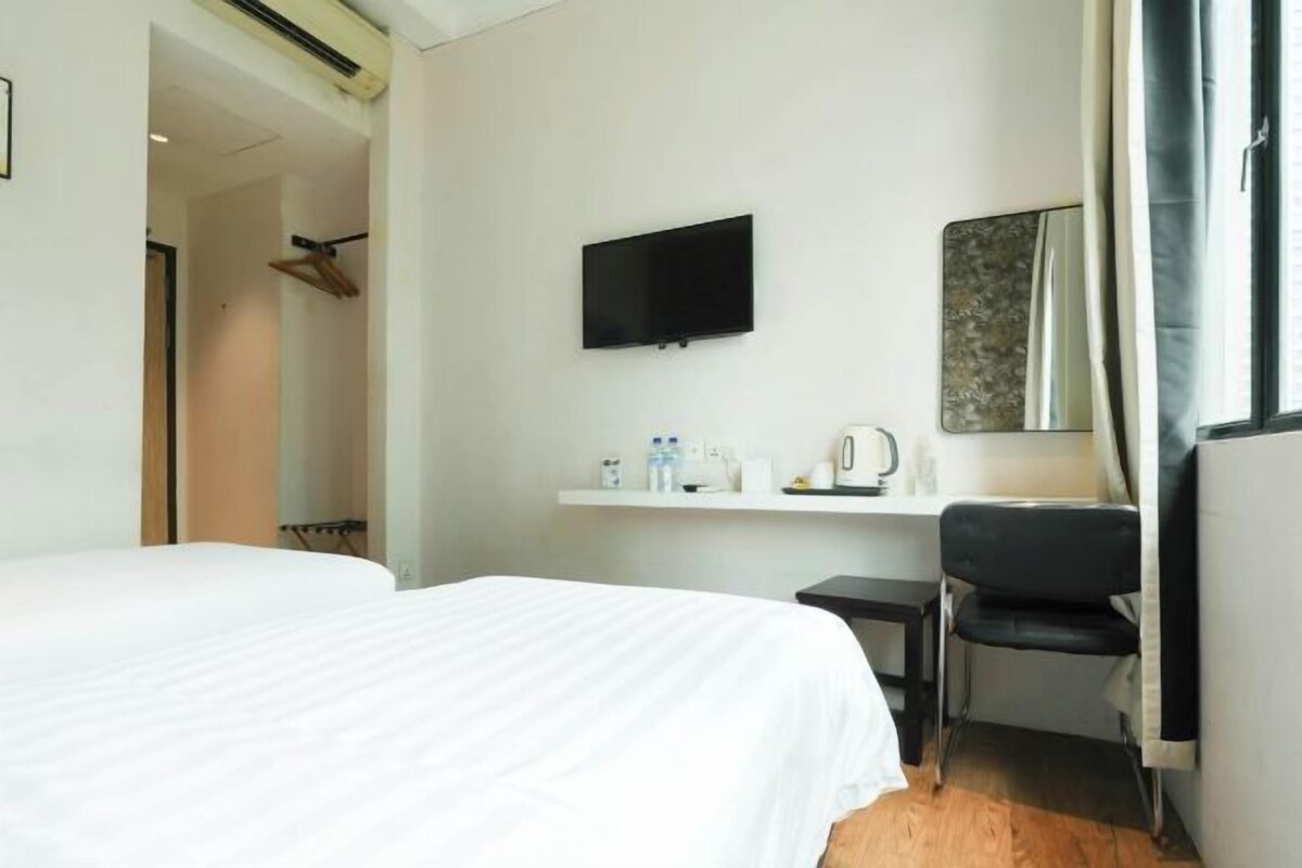 A hotel room with a bed, a desk, a chair, a TV, and a mirror.
