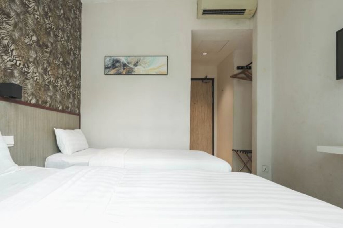 A hotel room with two beds, a wooden headboard, a painting on the wall, and a door leading to a bathroom.