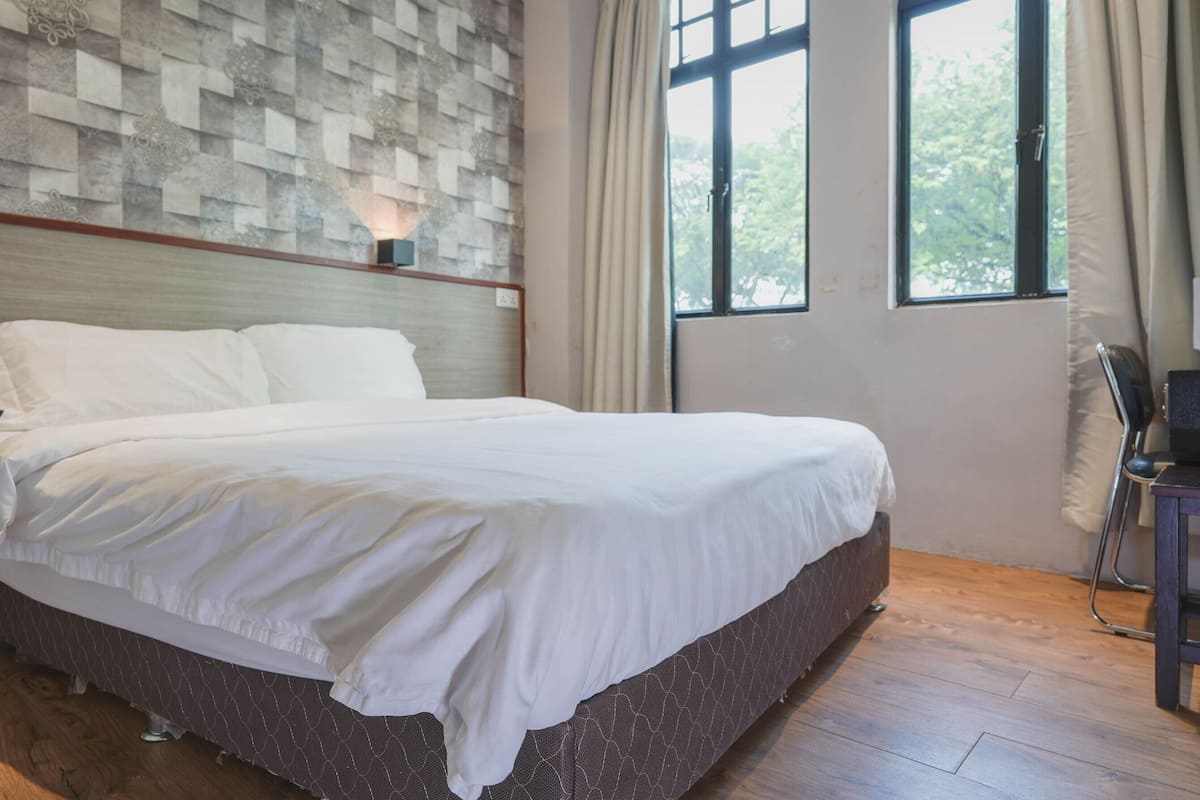 Cama bem arrumada em quarto com parede estampada, janela com cortinas e piso de madeira.