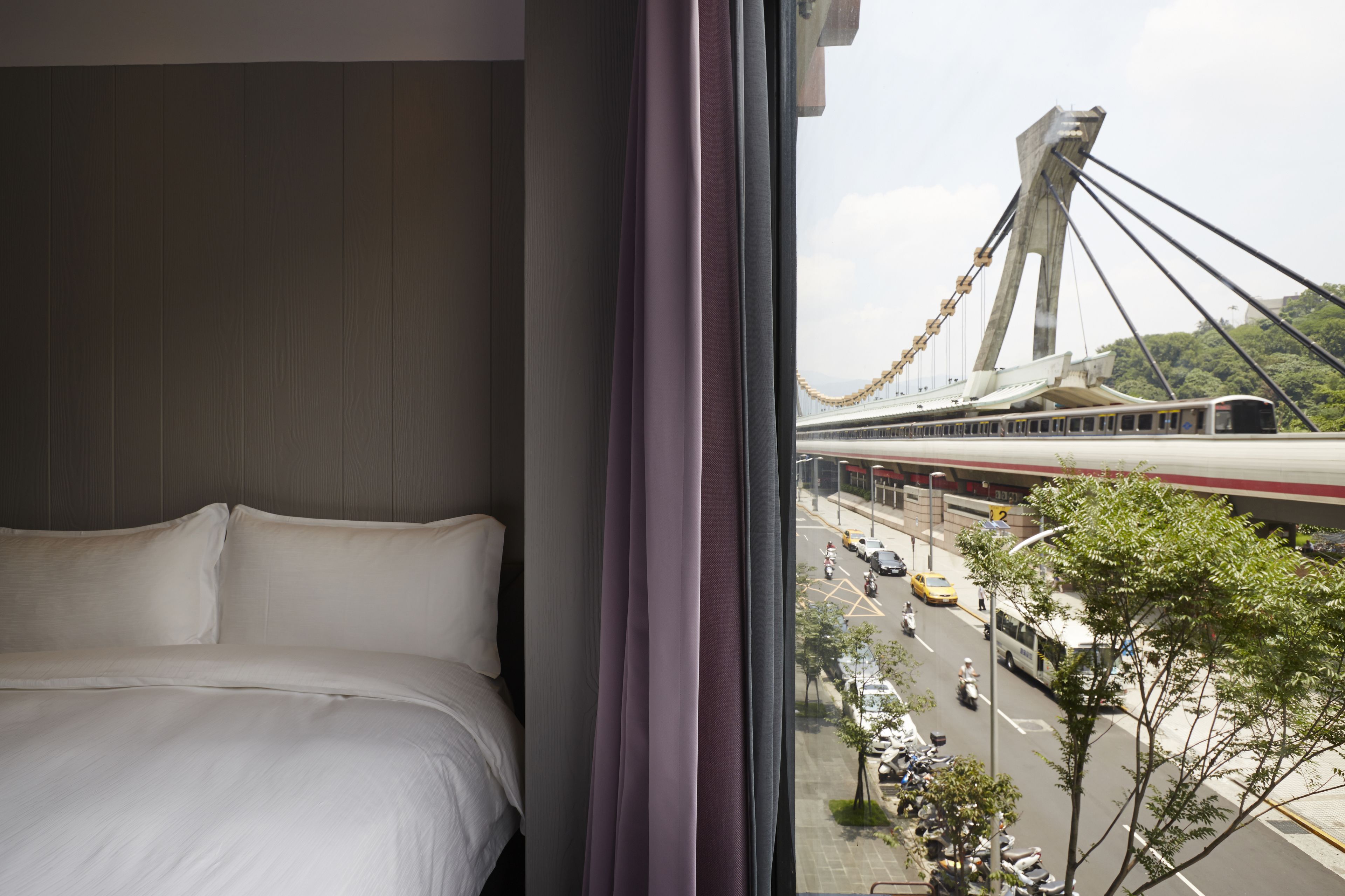 A hotel room with a bed and a view of a bridge and traffic.