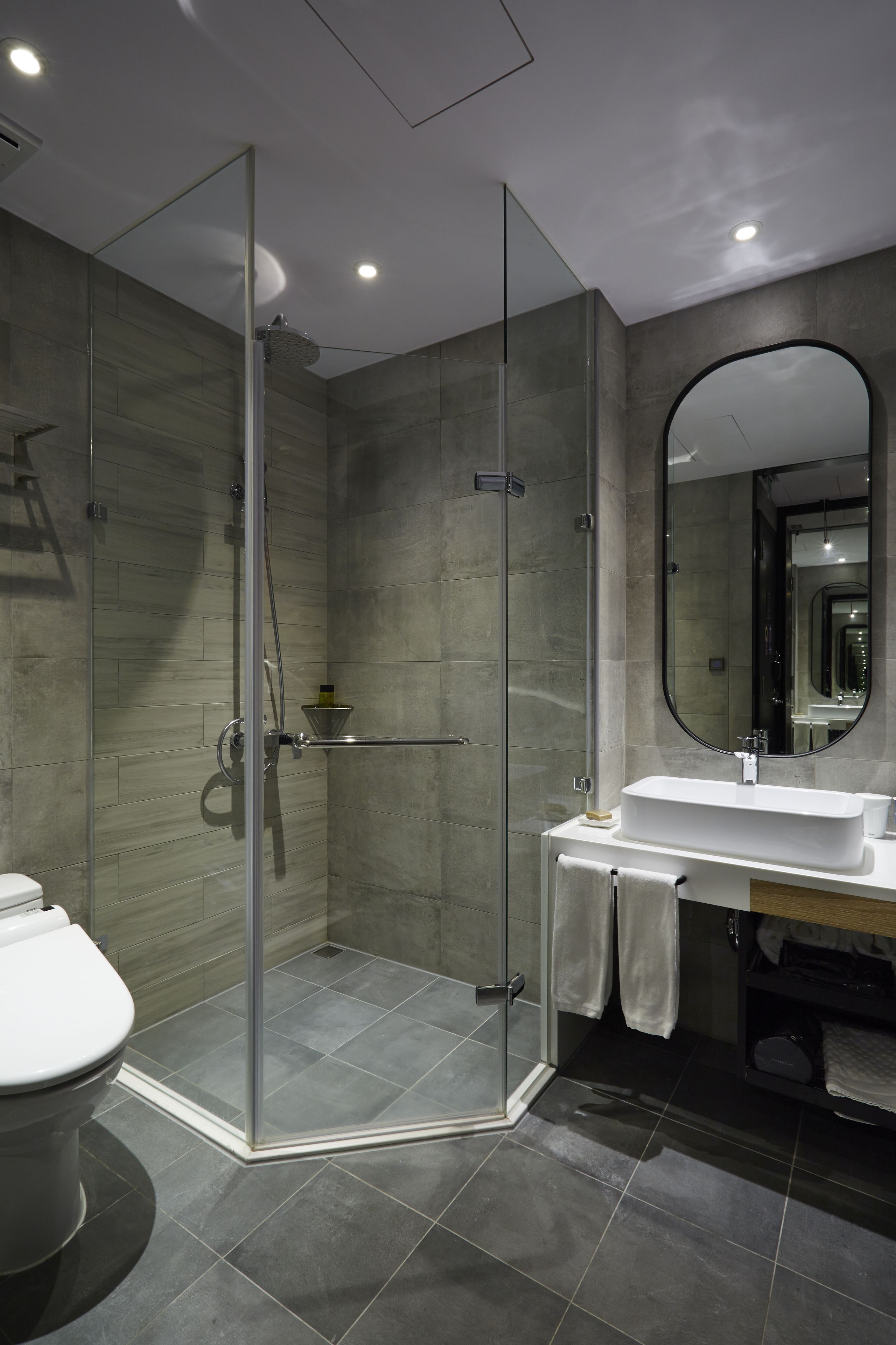 Un bany modern amb plat de dutxa envoltat de vidre, un lavabo blanc i un mirall gran.