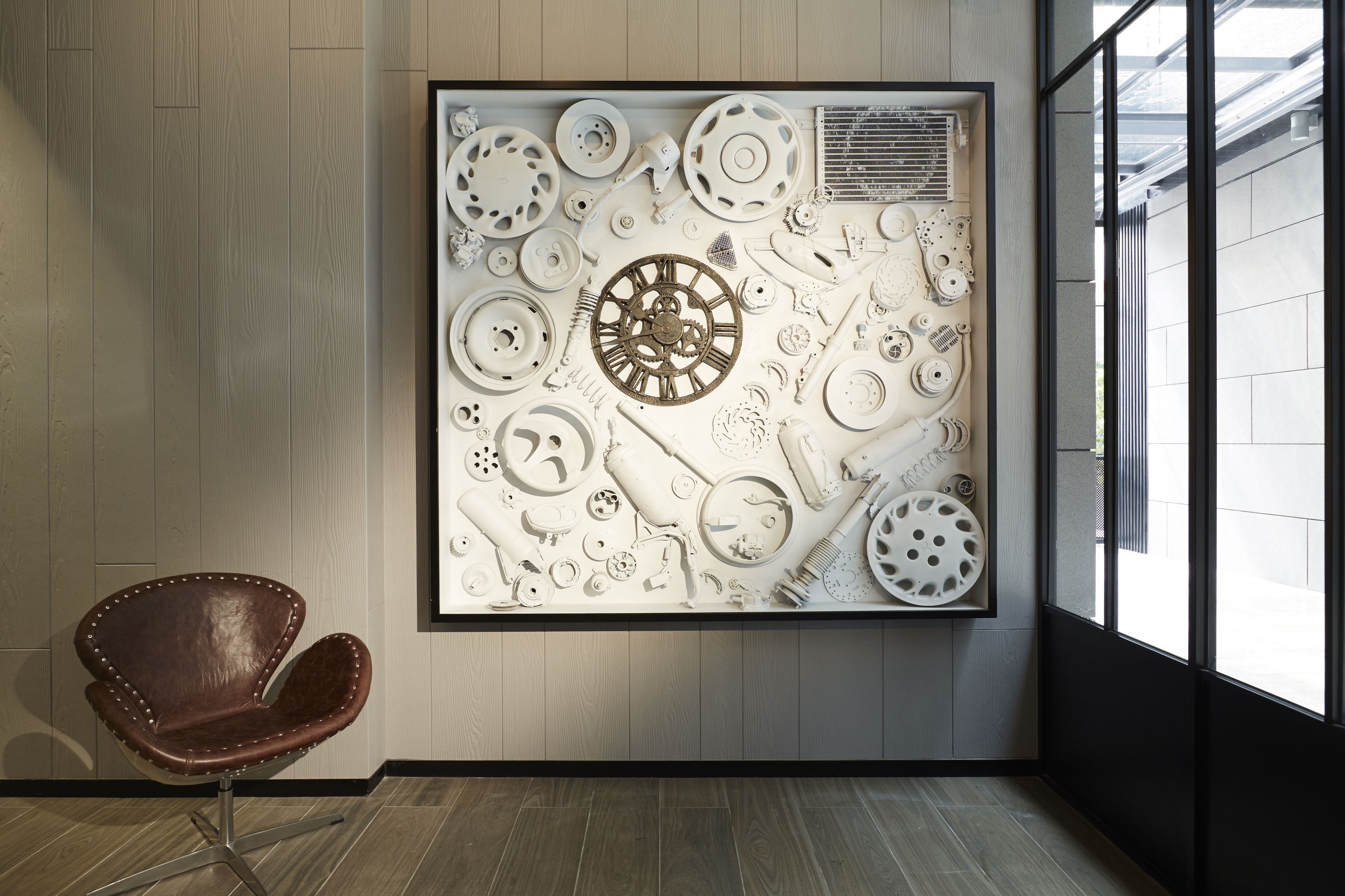 Een modern interieur met een groot abstract kunstwerk aan de muur, een bruine lederen fauteuil en uitzicht door een groot raam.