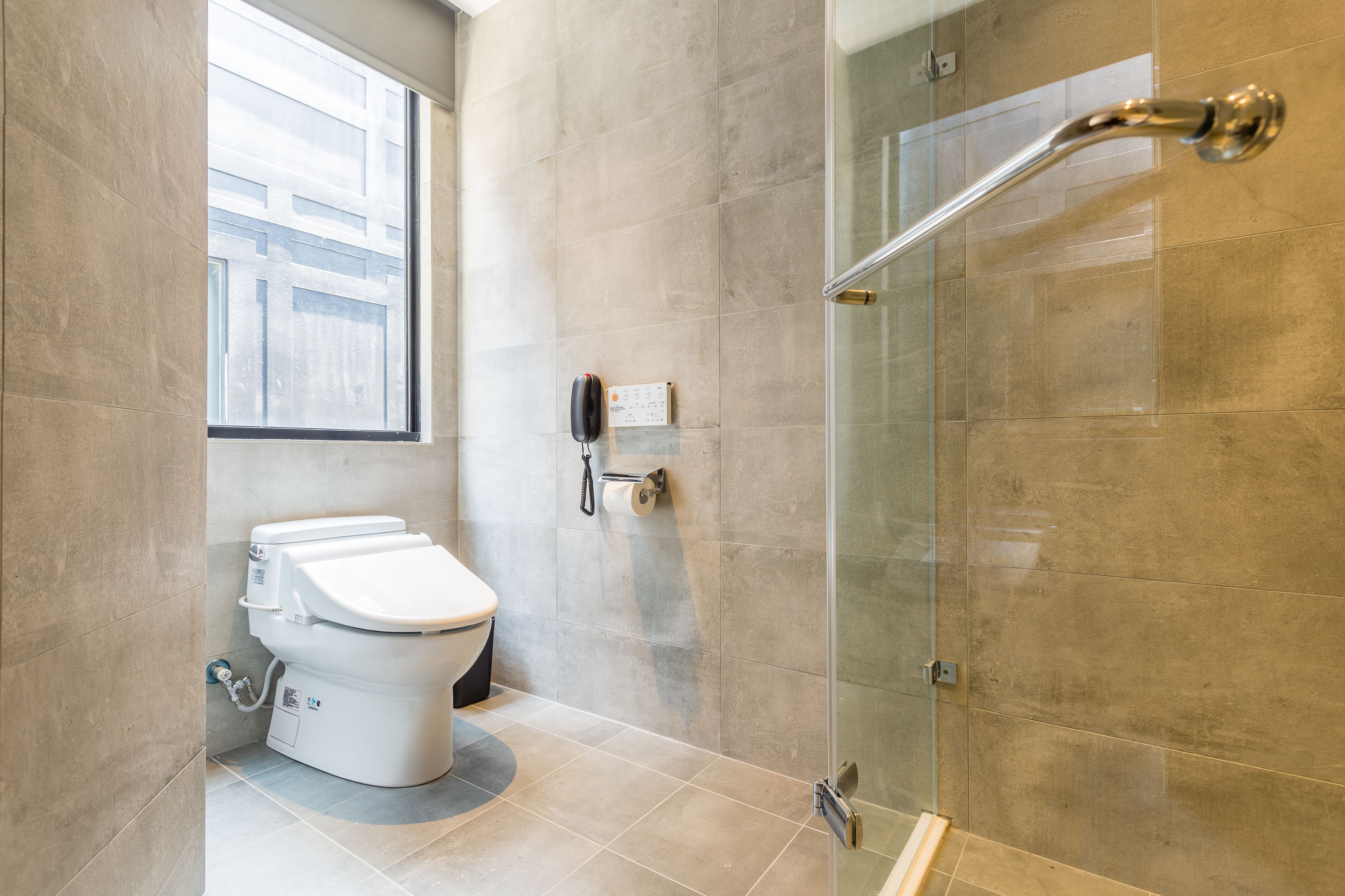A modern bathroom with a toilet, a glass shower enclosure, and a window providing natural light.