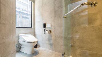 A modern bathroom with a toilet, a glass shower enclosure, and a window providing natural light.