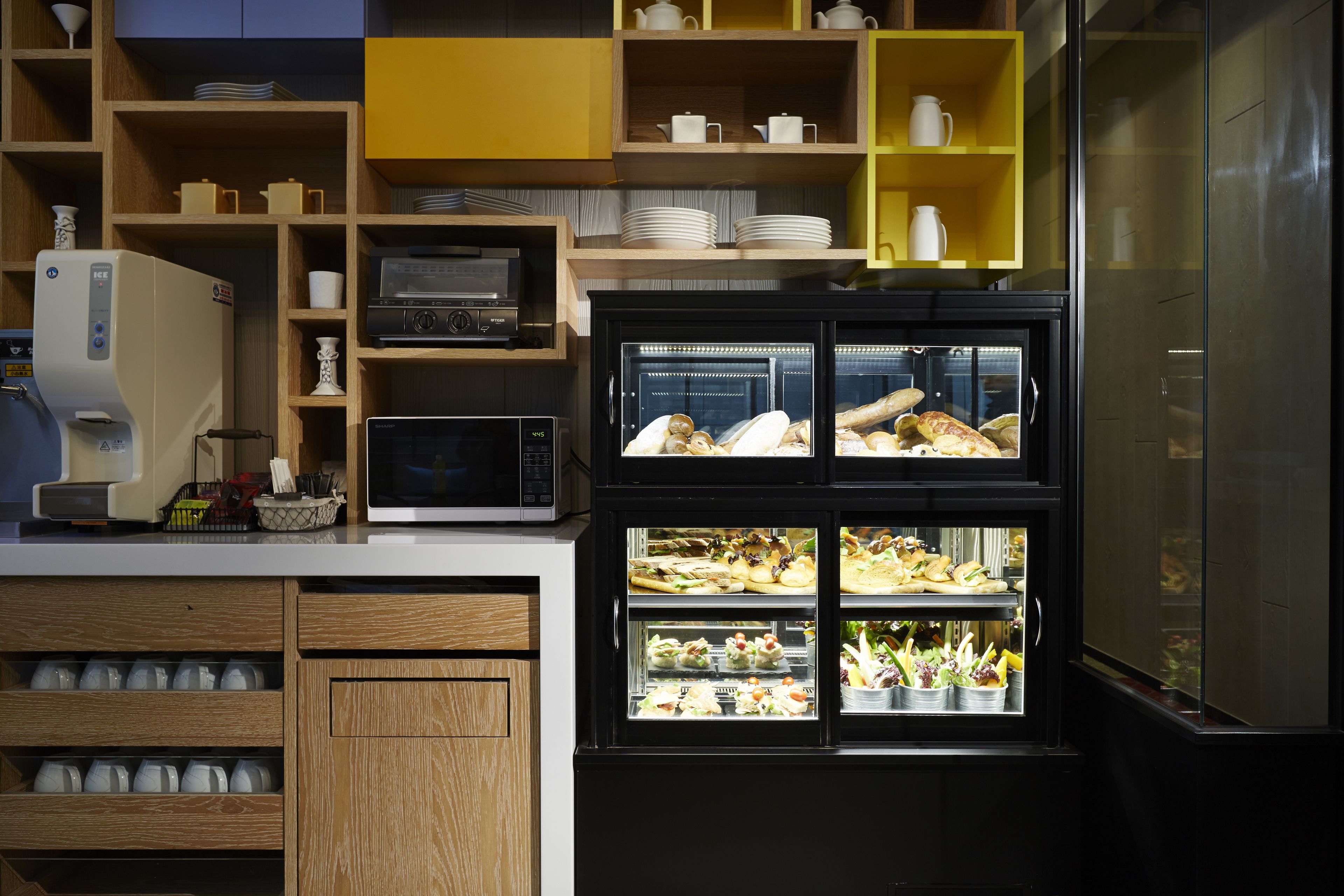 Una cocina con armarios de madera, un microondas, una cafetera y una vitrina con alimentos.