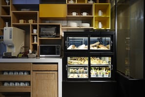 A kitchen with wooden cabinets, a microwave, a coffee machine, and a display case with food items. - Tango Inn Taipei JiHe (Taipei)
