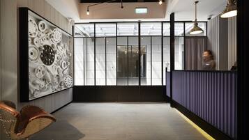 A modern reception area with a wooden floor, a seating area with a leather chair, a wall-mounted sculpture, and a reception desk with a dark panel.