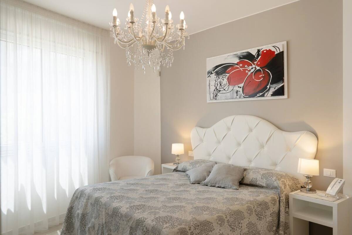 Un dormitorio con cabecera capitonada, dos mesitas de noche con lámparas, un candelabro y un cuadro abstracto grande en la pared.