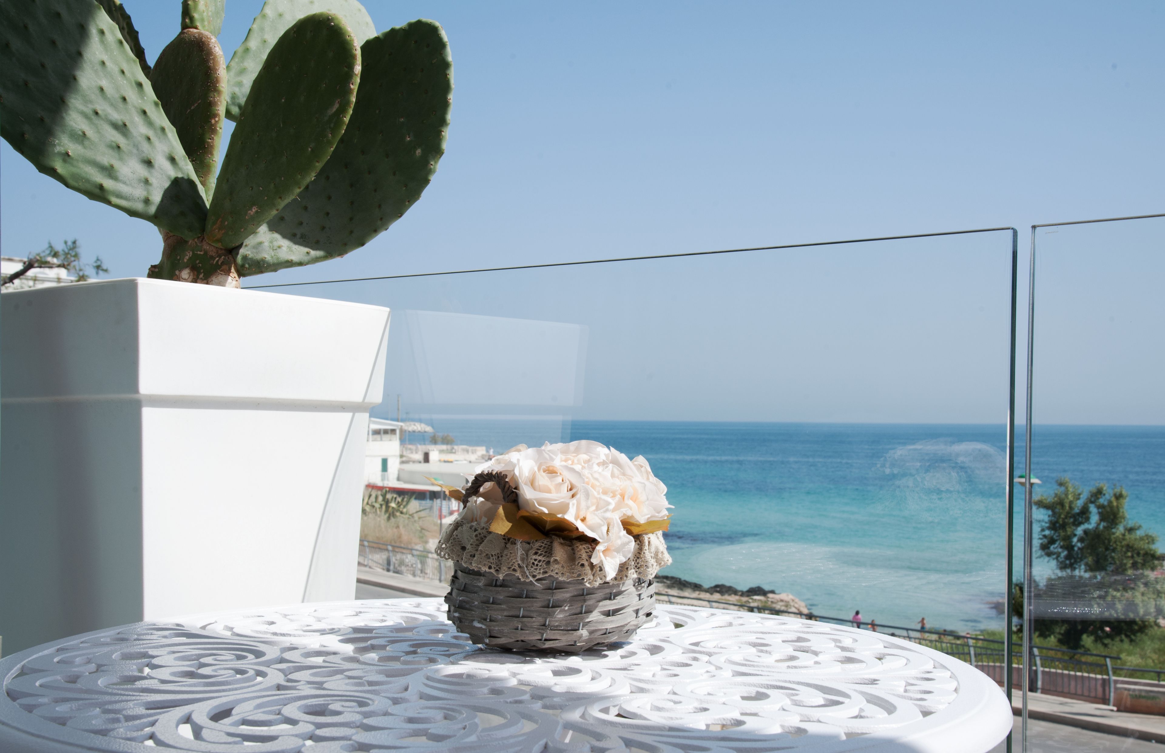 A white table with a decorative centerpiece, a cactus, and a view of the ocean.