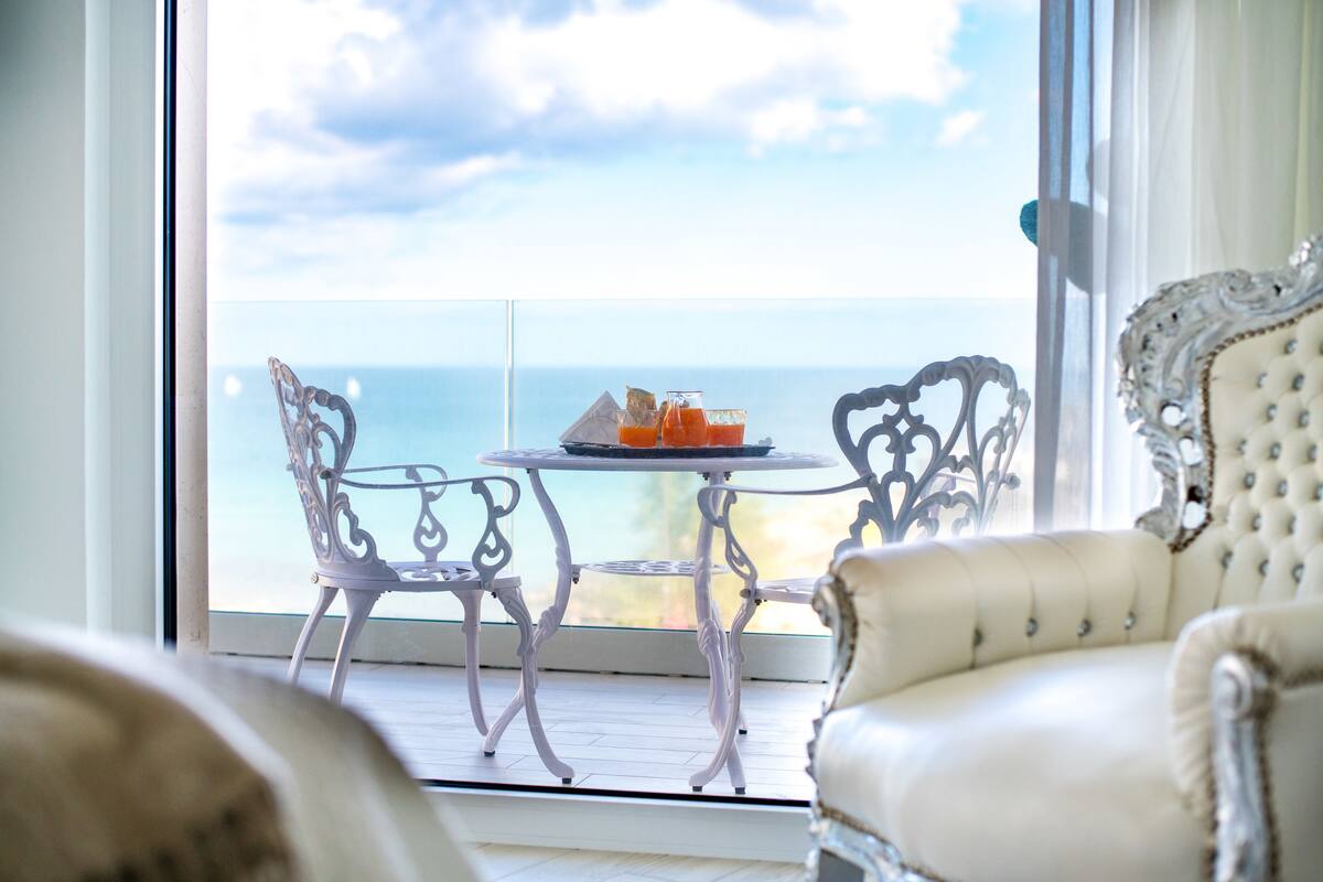 Un balcón con vista al mar, una mesa con bebidas y sillas decoradas.