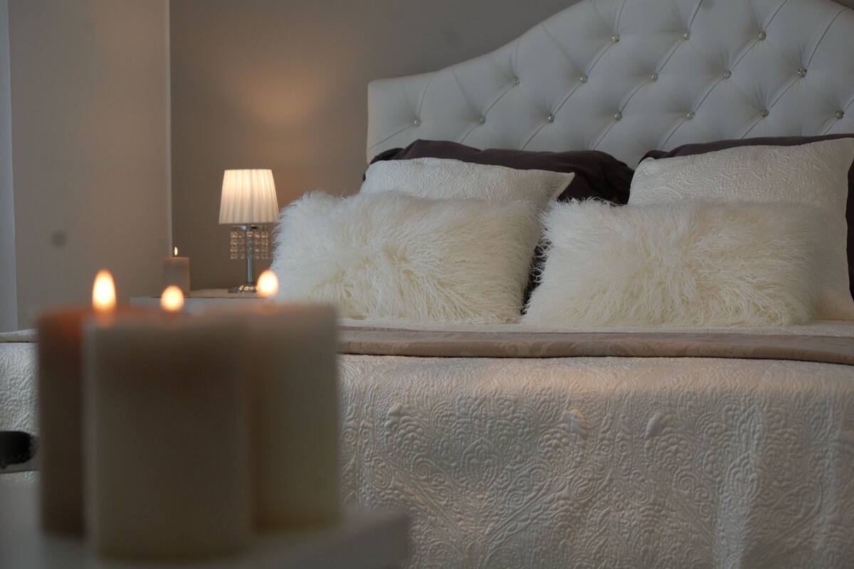Un dormitorio con un cabecero capitonado, almohadas mullidas y una vela encendida sobre la mesita de noche.