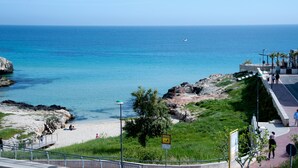 Vista costera con una playa arenosa, afloramientos rocosos y un mar azul cristalino.