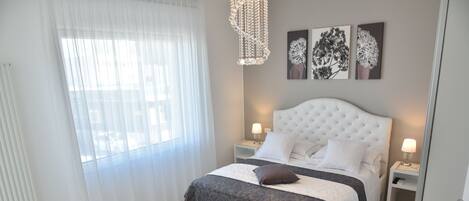 Un dormitorio con una cama blanca, dos mesitas de noche con lámparas, un candelabro y obras de arte en la pared.
