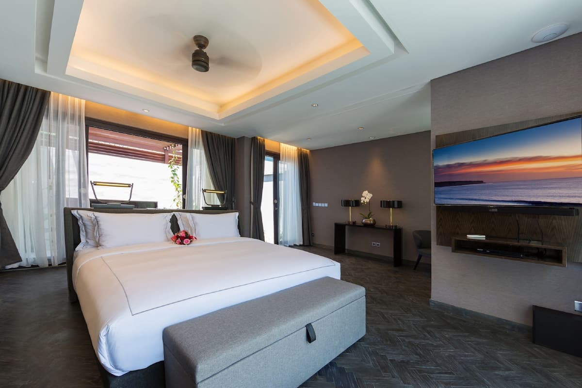 Una habitación de hotel moderna con una cama grande, un televisor de pantalla plana en la pared y vista al océano a través de la ventana.
