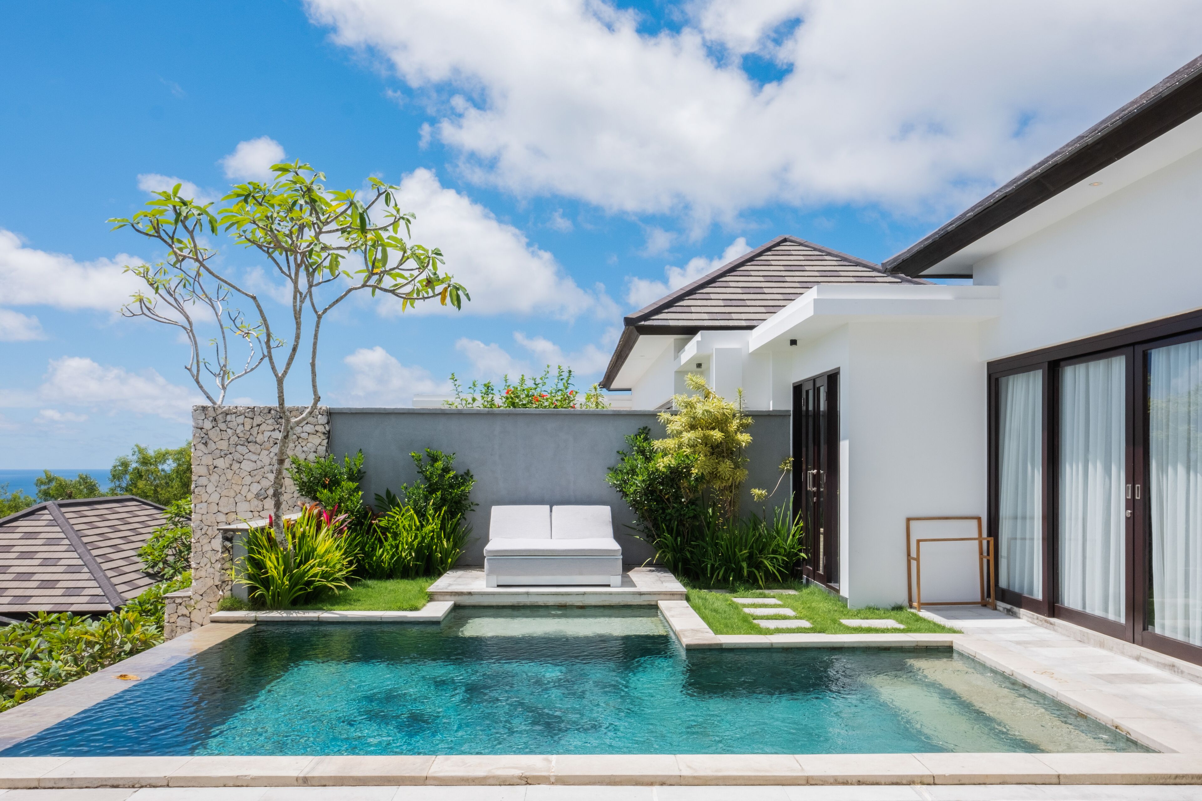 A modern house with a swimming pool, a stone wall, and a garden.