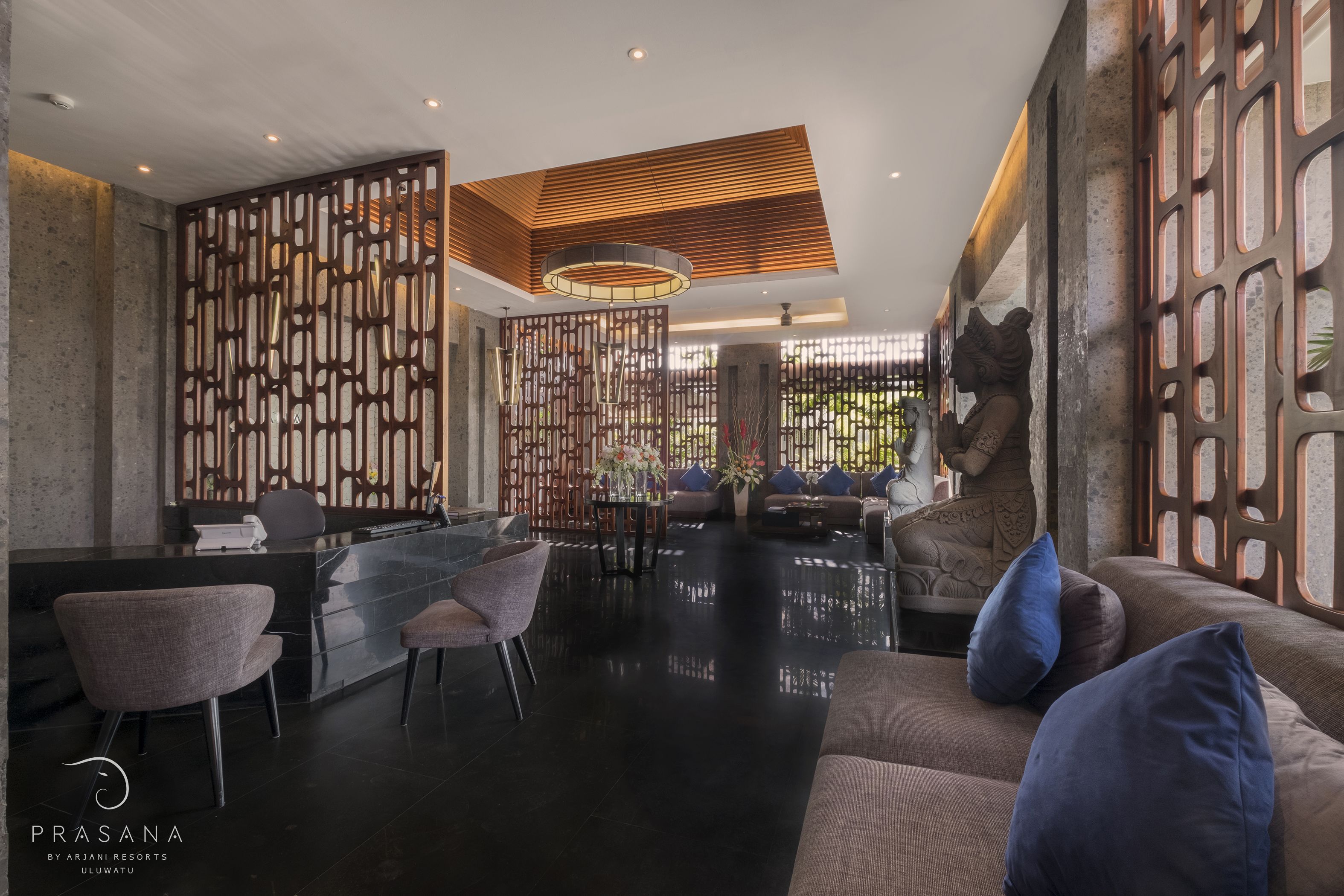 A modern reception area with a black reception desk, grey chairs, a wooden partition, and a sofa with blue cushions.