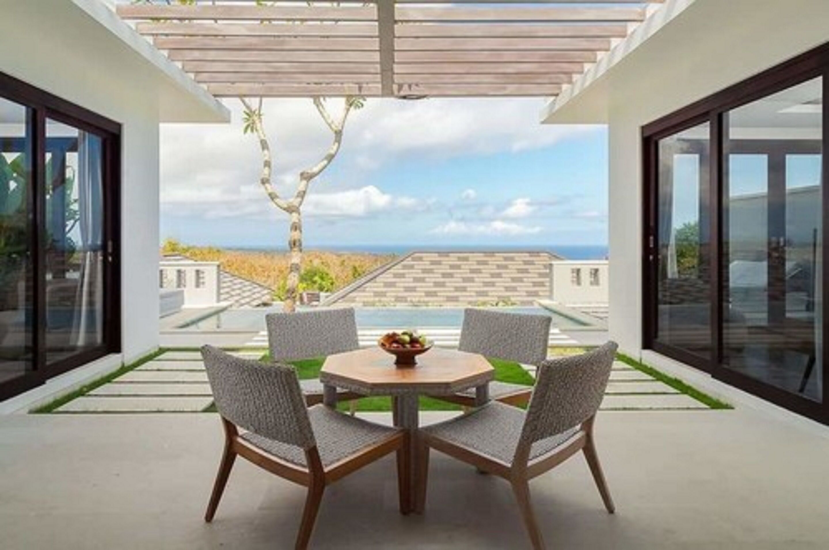 En moderne udendørs terrasse med et rundt bord og fire stole, med udsigt over strand og hav.