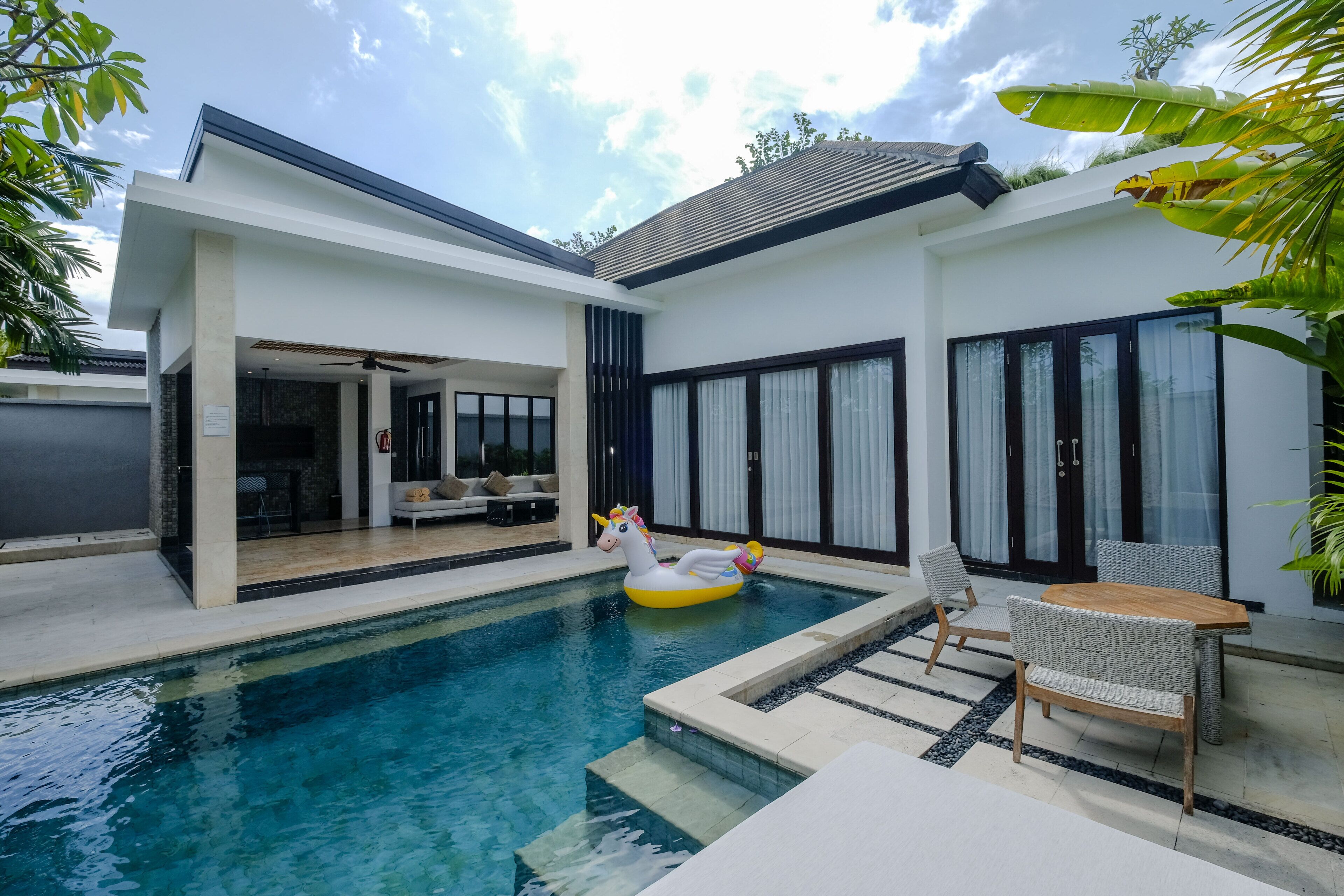 Une maison moderne dotée d’une piscine, d’un flotteur en forme de licorne et d’un espace salon extérieur.