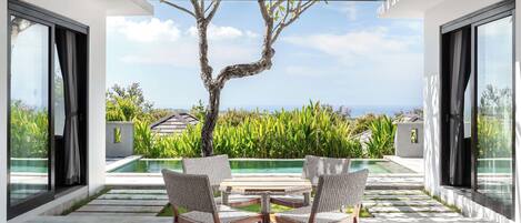 A modern outdoor patio with a pool, wicker chairs, and a view of the ocean.