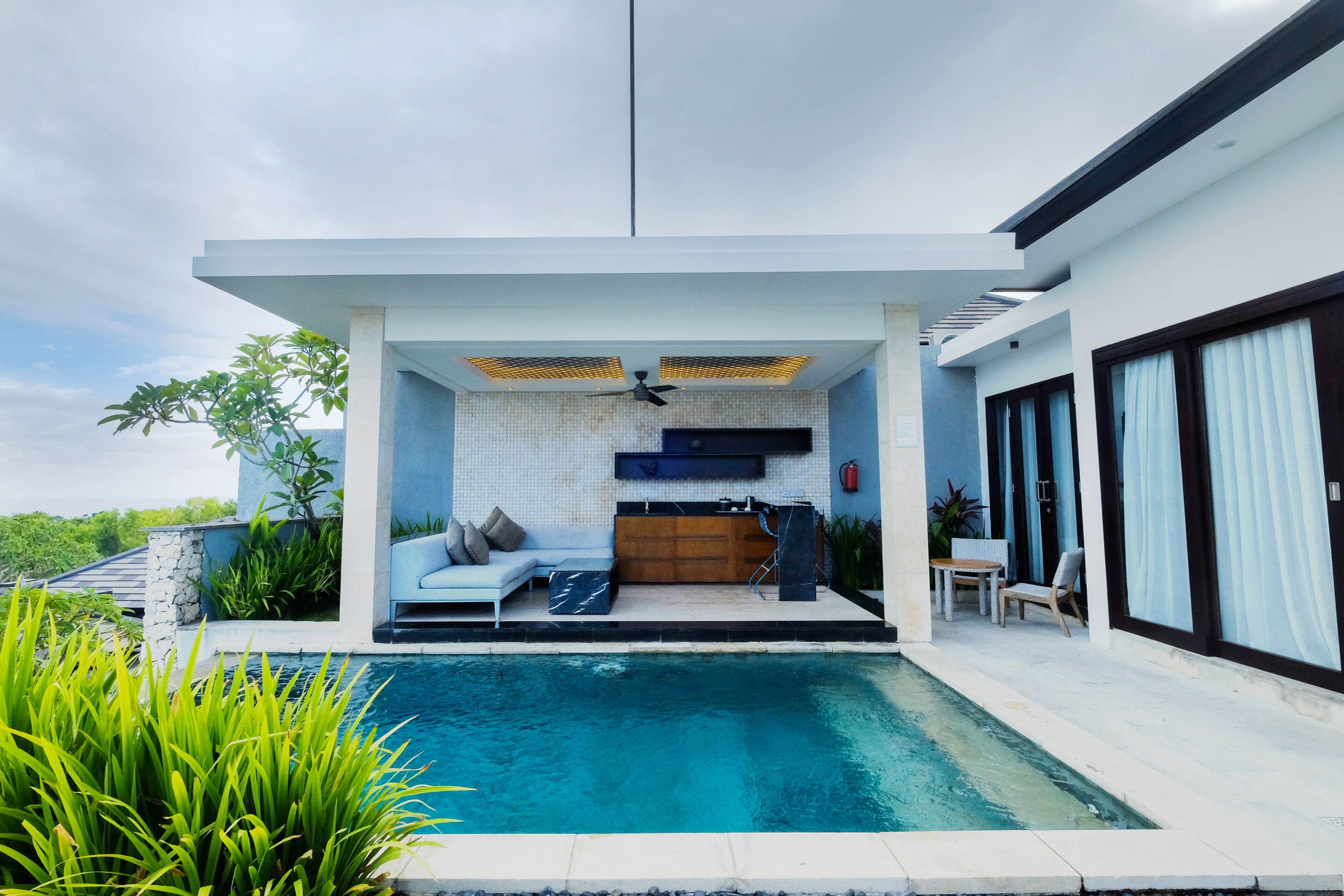 Una casa moderna con piscina, cocina integrada y una zona de estar con sofá y sillones.