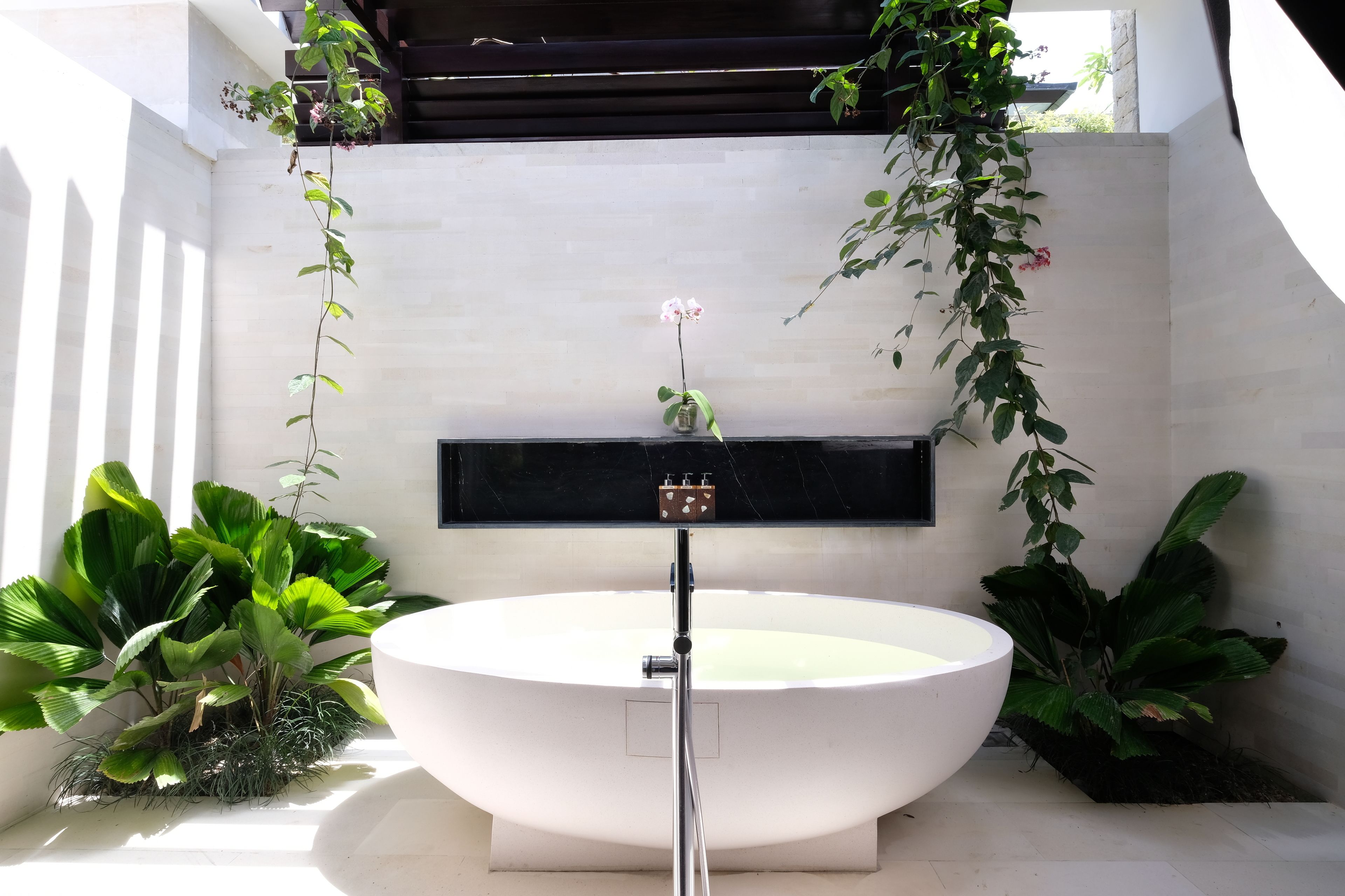 A modern bathroom with a freestanding bathtub, a wall-mounted sink, and various potted plants.
