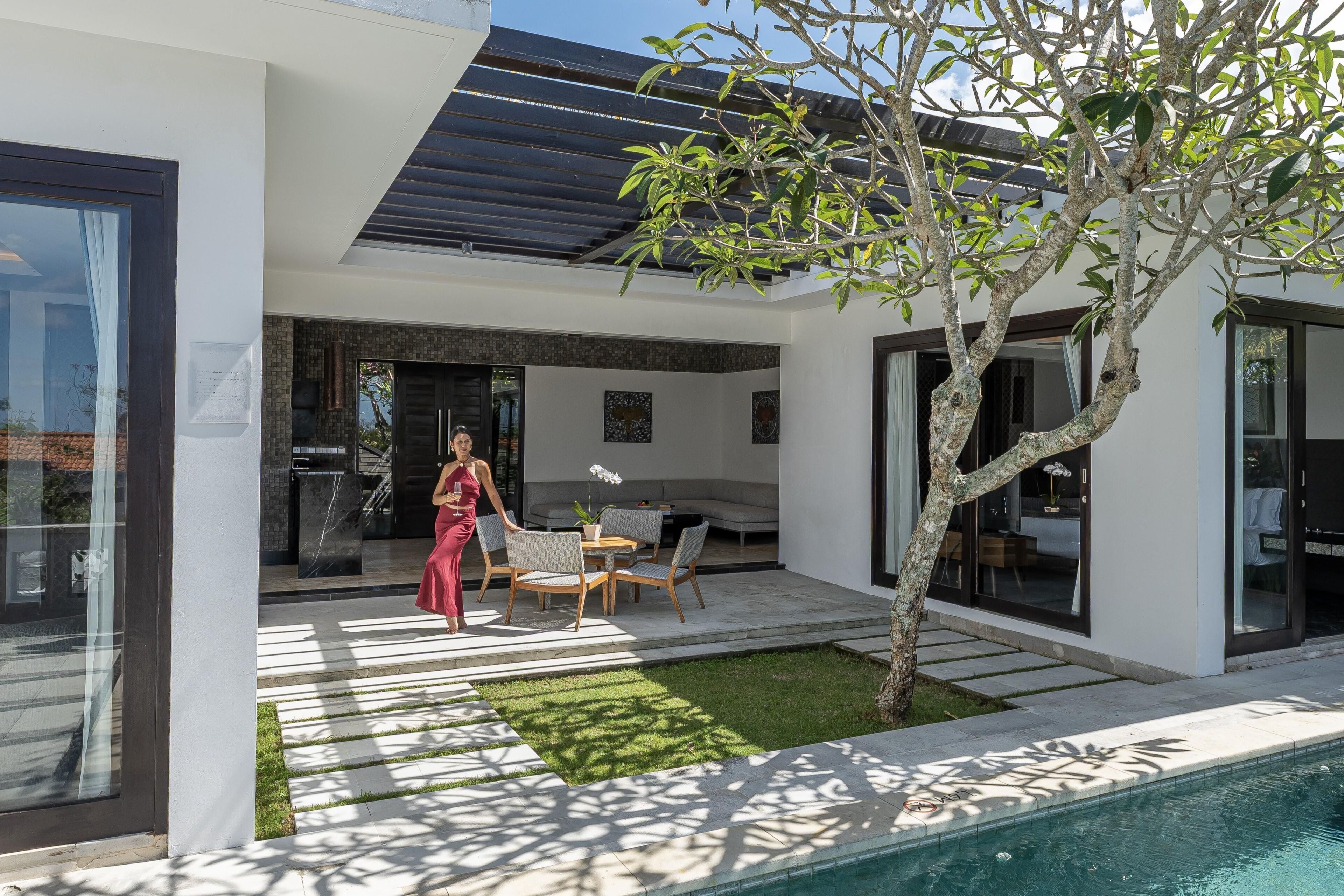 A modern house with a pool, outdoor seating, and a tree.