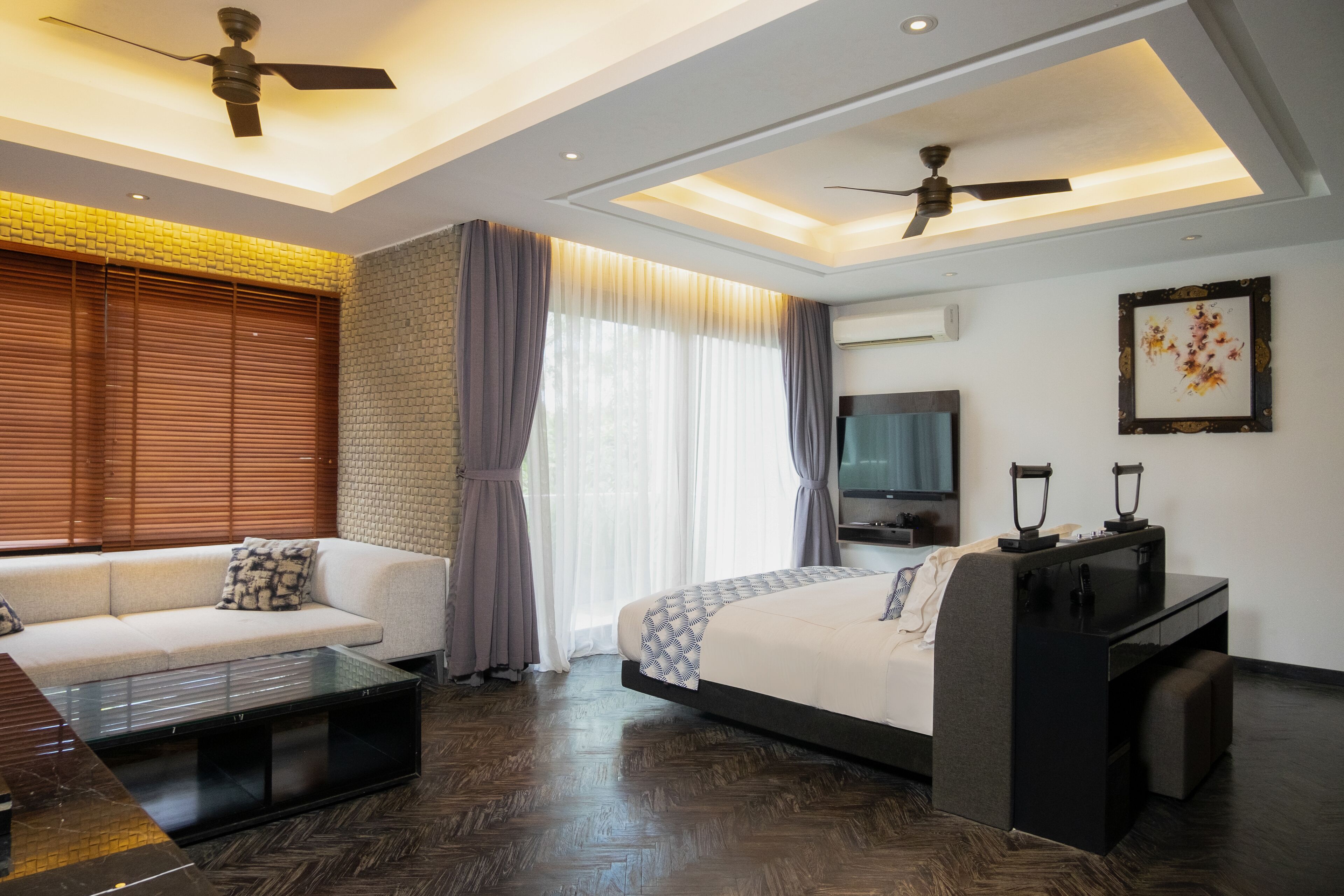 A modern hotel room with a sofa, a bed, a desk, and a ceiling fan.