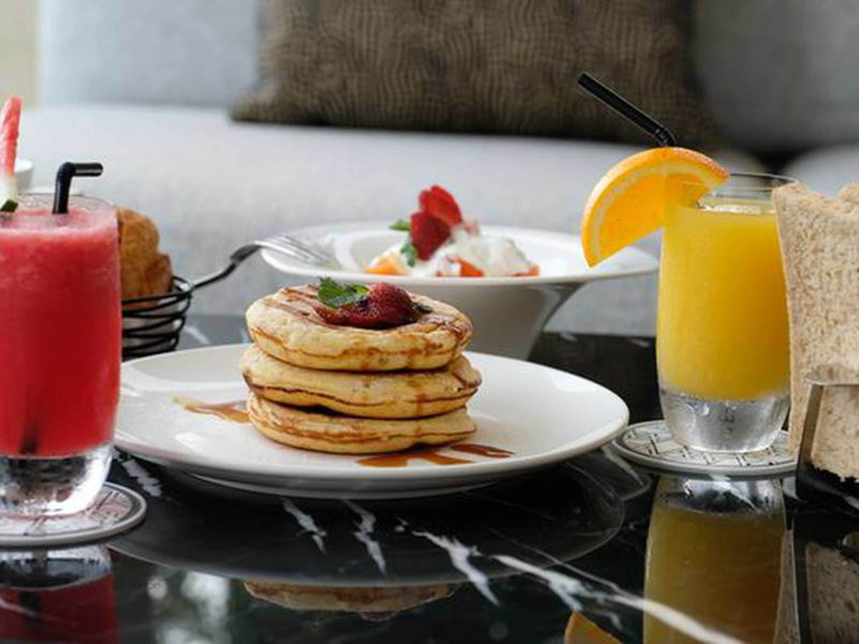 A breakfast setting with pancakes, a smoothie, and orange juice on a table.