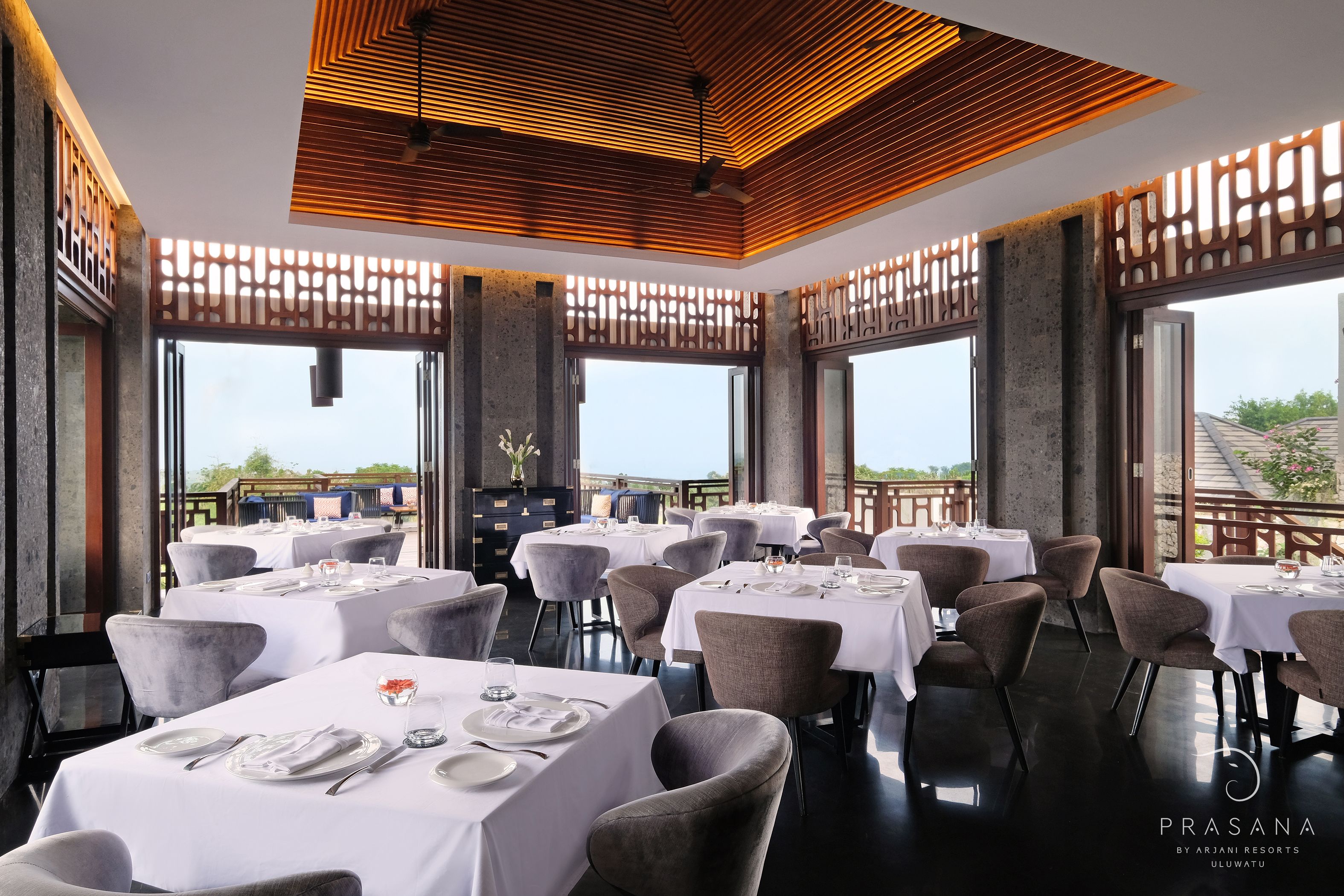 A restaurant with multiple tables set for dining, large windows, and a modern ceiling design.
